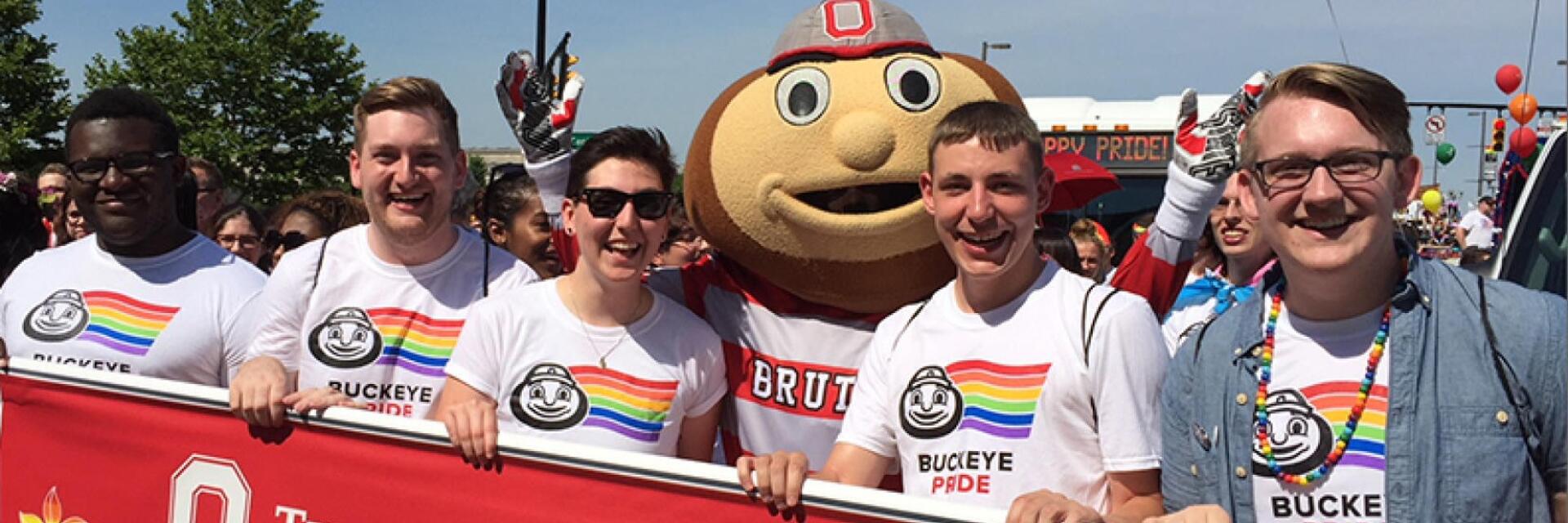 People marching in an LGBTQ Pride March with the mascot Brutus Buckeye